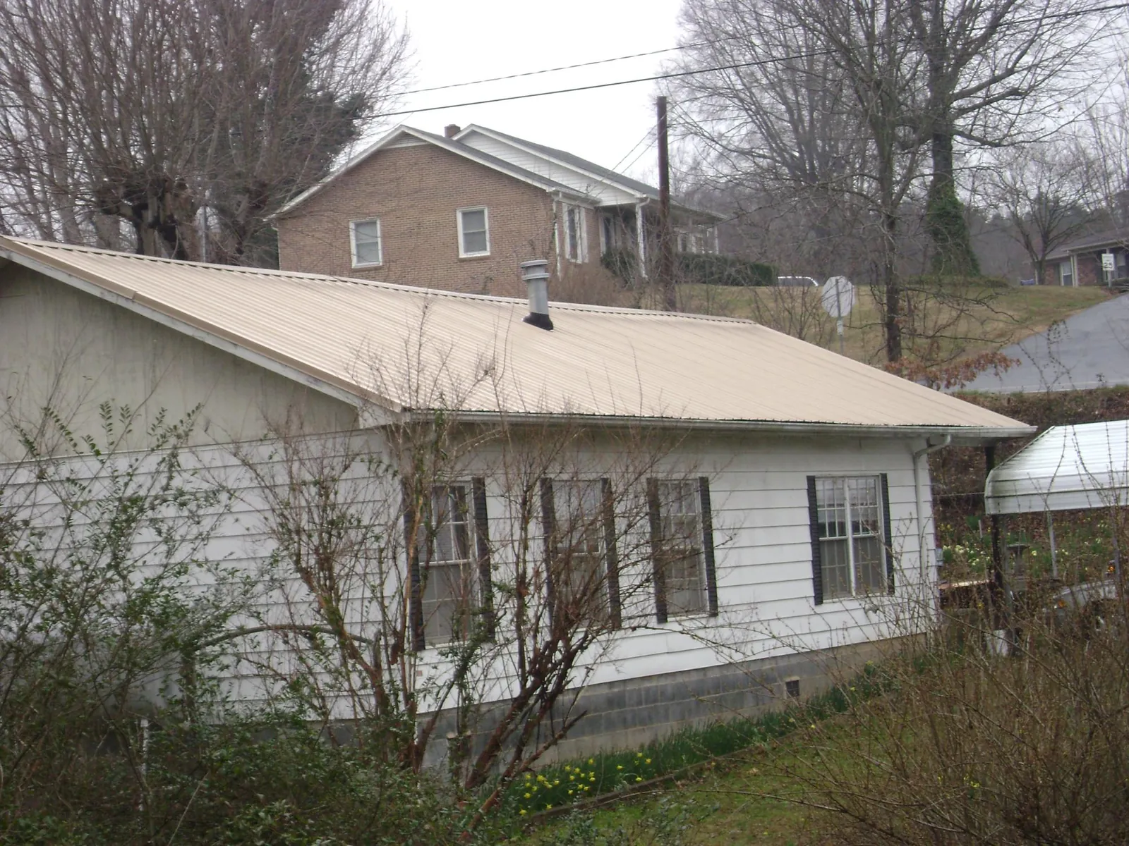 Tan metal roof on a white sided house set into a hillside — Commercial Roofing by Roofing Brothers in Sparks Glencoe